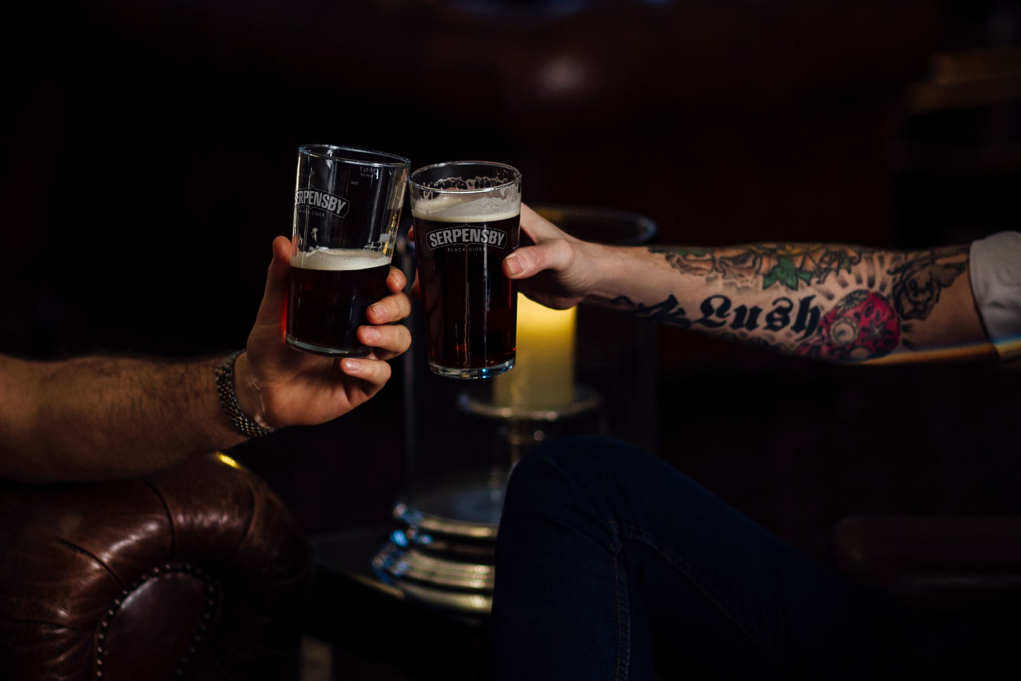 Two people raising SERPENSBY glasses filled with black cider.
