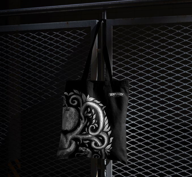 Black SERPENSBY tote bag hanging against a metal grille.